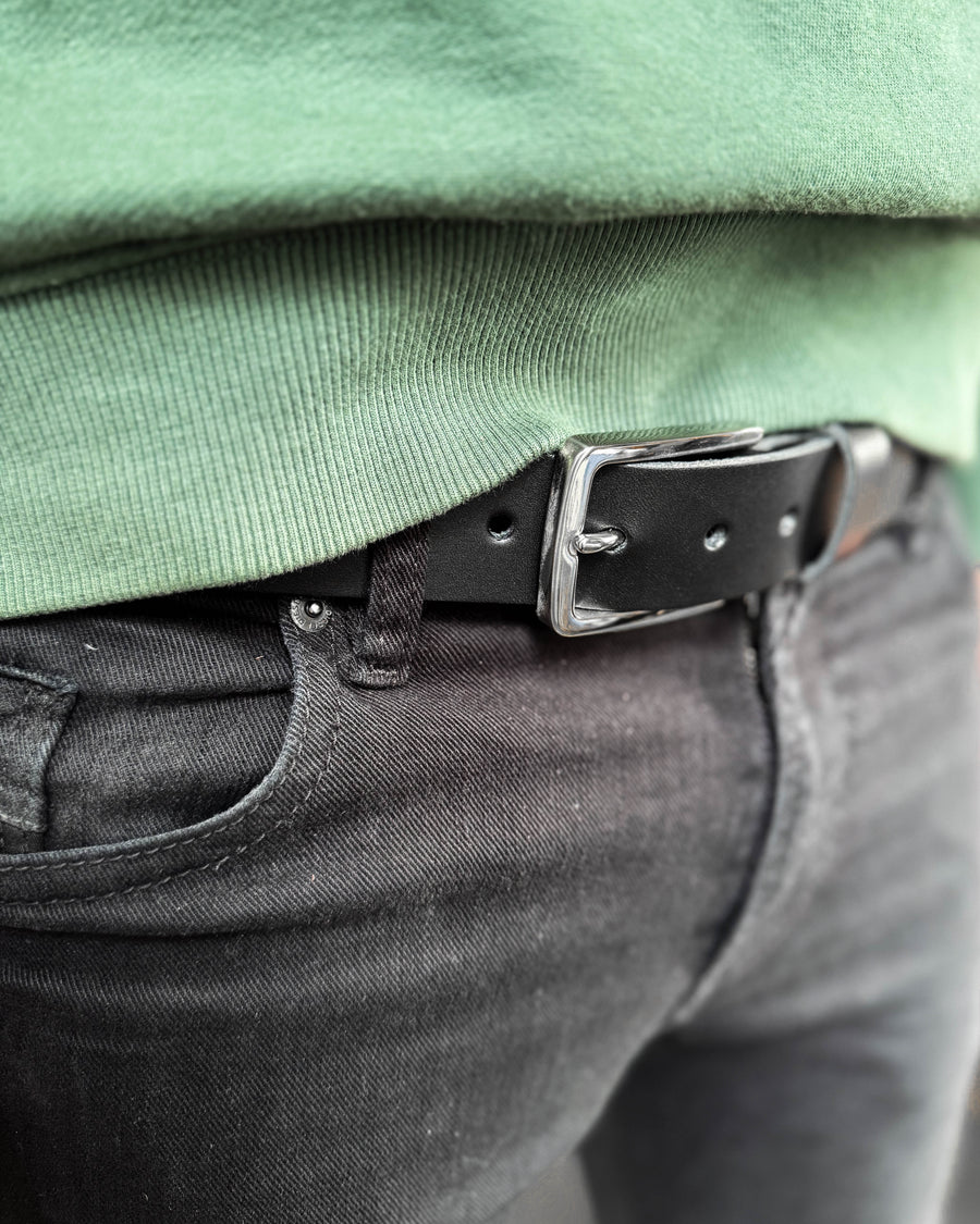 EDGE Gürtel aus schwarzem Leder mit silberfarbener Stahlschnalle, getragen zu schwarzer Jeans mit grünem Sweatshirt