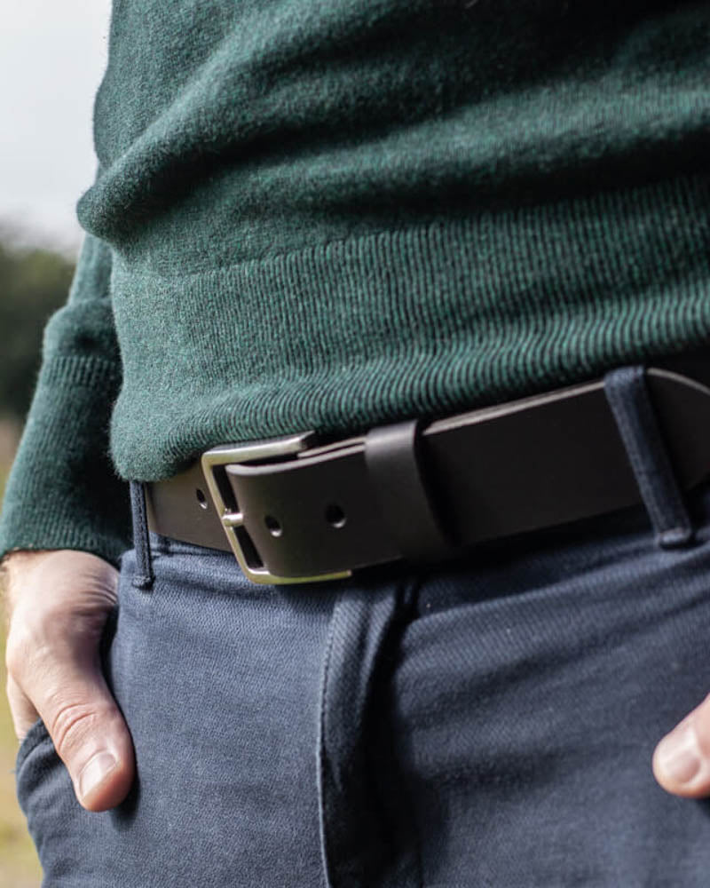EDGE Gürtel aus schwarzem Leder mit Stahlschnalle, getragen zu blauer Hose mit dunkelgrünem Strickpullover im Freien