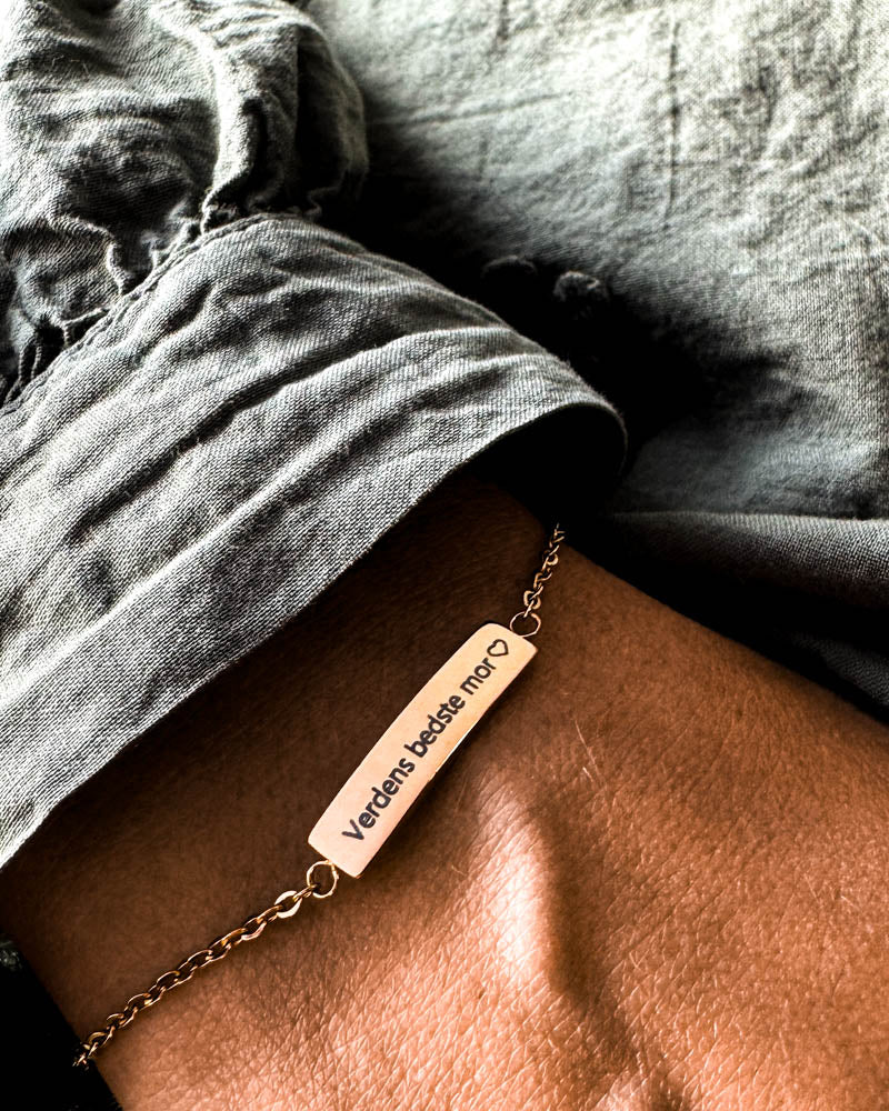 EVI Armband aus vergoldetem Edelstahl mit der Gravur "Verdens bedste mor" ♡ am Handgelenk, graues Leinenhemd