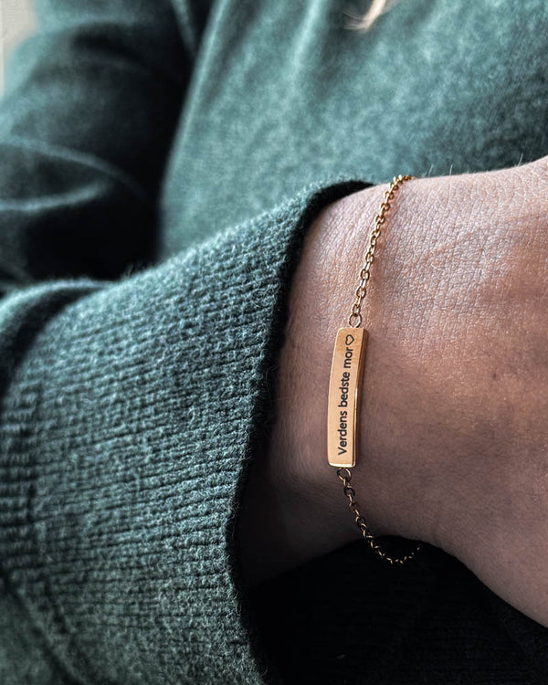 EVI Armband aus vergoldetem Edelstahl mit "Verdens bedste mor" ♡ auf länglicher Platte graviert, am Handgelenk zu grünem Strick getragen