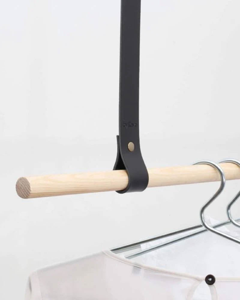 HOLD 15 Aufhängeschlaufe aus schwarzem Leder mit Niete um helle Holzstange mit Bügeln und weißer Bluse