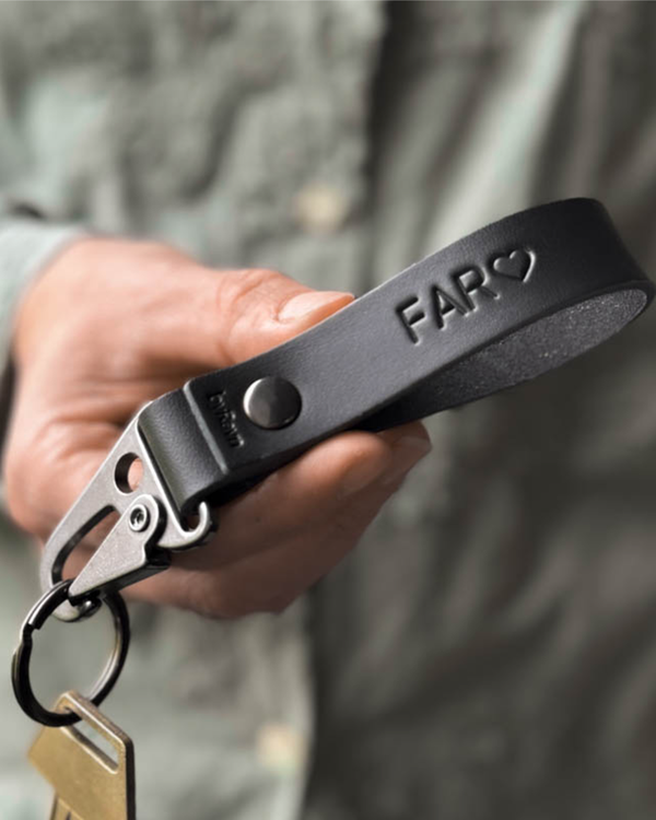 HOOK Schlüsselanhänger aus schwarzem Leder mit Karabiner aus Stahl und der Gravur "Far" ♡, in der Hand gehalten mit Schlüssel