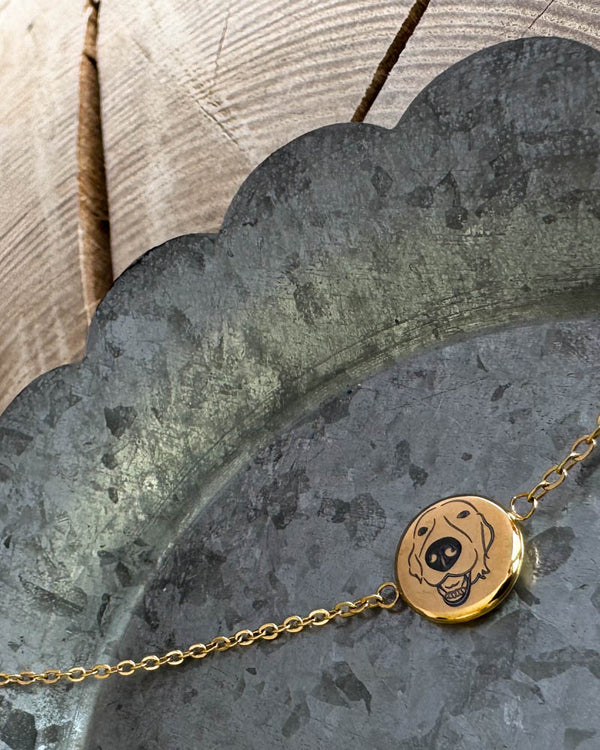 IBI PORTRAIT Armband aus vergoldetem Edelstahl mit gezeichnetem Hund auf runder Platte graviert, auf Zinkschale liegend