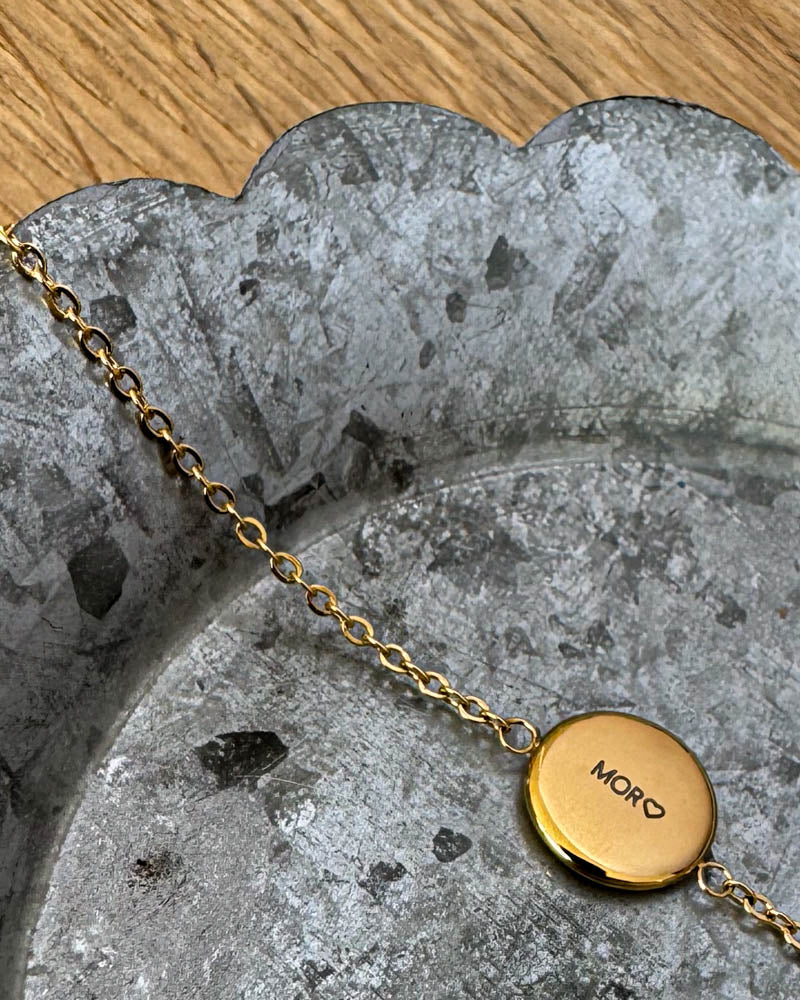 IBI QUOTE Armband aus vergoldetem Edelstahl mit der Gravur "Mor" ♡ auf runder Platte, auf Zinkschale liegend