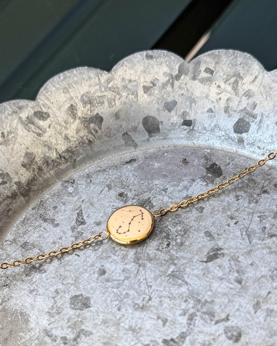 IBI STAR Armband aus vergoldetem Edelstahl mit dem Sternbild Skorpion auf runder Platte graviert, auf Zinkschale liegend