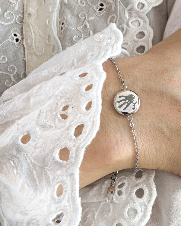 IBI MOTIF Armband aus silberfarbenem Edelstahl mit graviertem Handabdruck, am Handgelenk zu weißer Spitzenbluse getragen