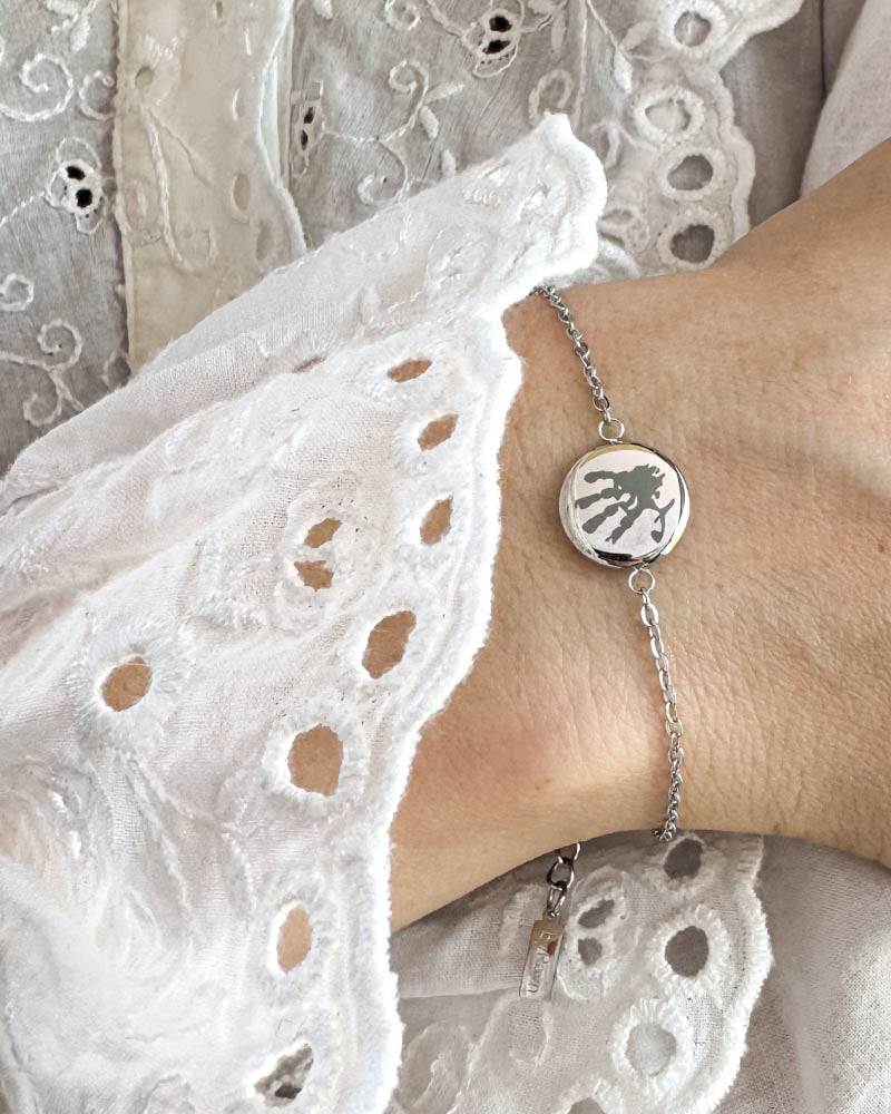 IBI MOTIF Armband aus silberfarbenem Edelstahl mit graviertem Handabdruck, am Handgelenk zu weißer Spitzenbluse getragen