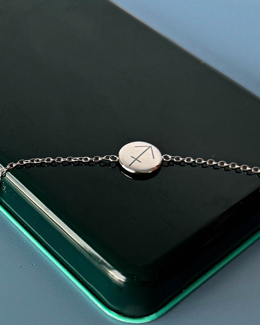 IBI STAR Armband aus silberfarbenem Edelstahl mit Sternzeichen Schütze auf runder Platte graviert, auf dunkelgrüner Schachtel liegend