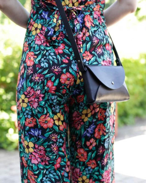 INA Schultertasche aus schwarzem Leder, als Crossbody getragen zu geblümtem Jumpsuit im Garten
