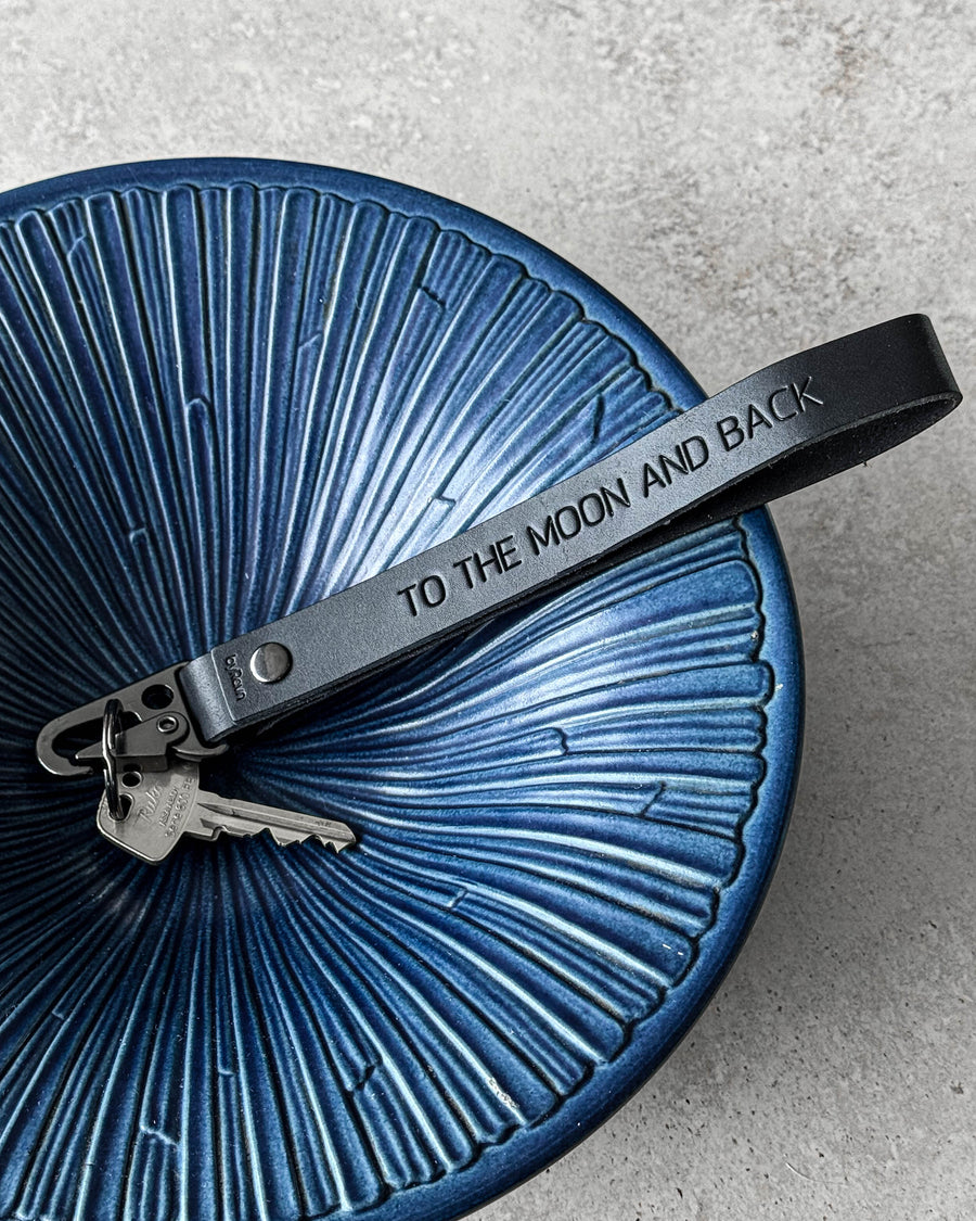 IRON Schlüsselanhänger aus schwarzem Leder mit der Gravur "To the moon and back" und Schlüsseln in blauer geriffelter Keramikschale