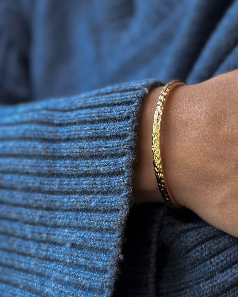 LUNA Armband aus vergoldetem Edelstahl, gehämmerter Armreif am Handgelenk zu blauem Strick getragen