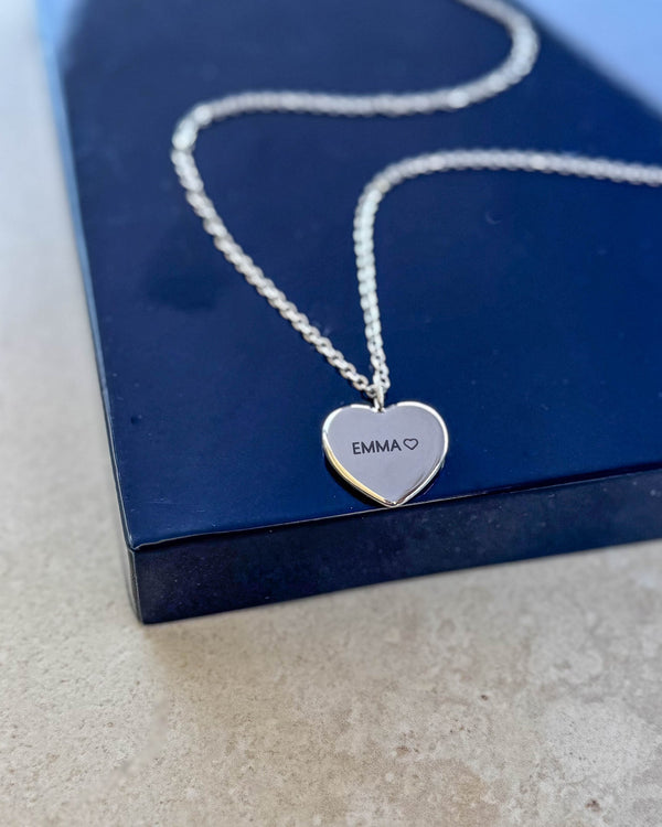 LUV QUOTE Namenskette aus silberfarbenem Edelstahl mit Gravur "EMMA" ♡ auf Herzanhänger, liegend auf dunkelblauer Geschenkbox