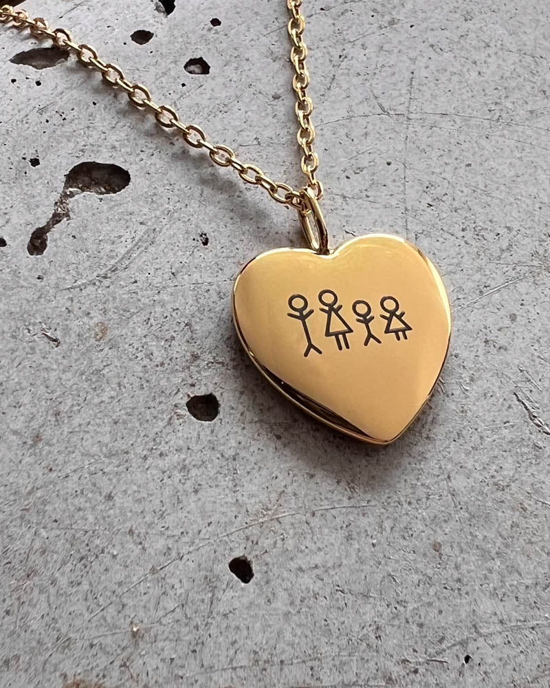 LUV STICK Halskette aus vergoldetem Edelstahl, Herzanhänger mit gravierter vierköpfiger Streichholz-Familie, liegend auf rohem Beton