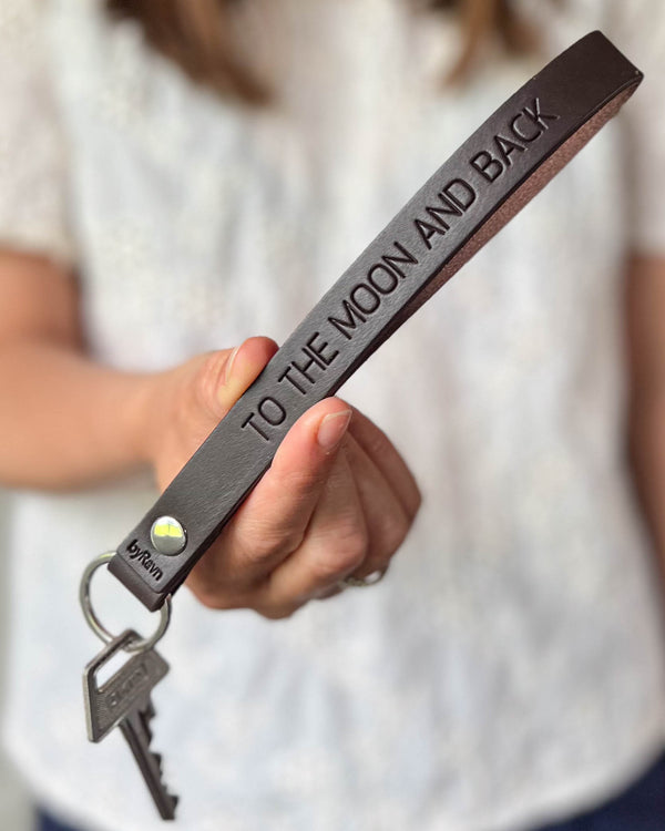LUX Schlüsselanhänger aus dunkelbraunem Leder mit persönlicher Gravur "To the moon and back", in der Hand gehalten mit Schlüsseln