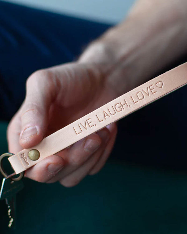 LUX Schlüsselanhänger aus naturfarbenem Leder mit Messingniete und persönlicher Gravur "Live, laugh, love" ♡, in der Hand gehalten mit Schlüssel