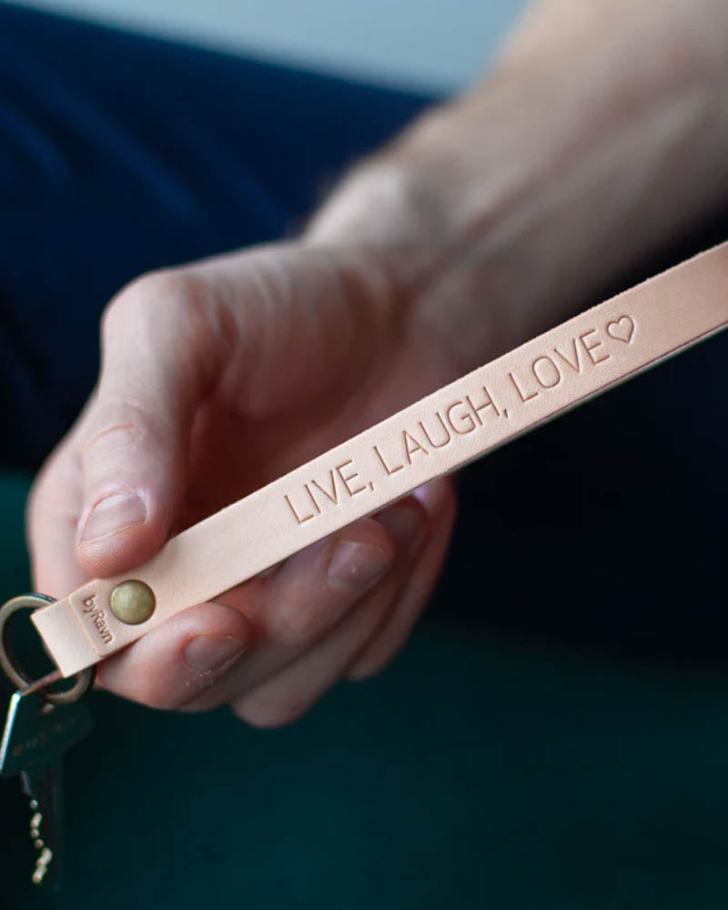 LUX Schlüsselanhänger aus naturfarbenem Leder mit Messingniete und persönlicher Gravur "Live, laugh, love" ♡, in der Hand gehalten mit Schlüssel