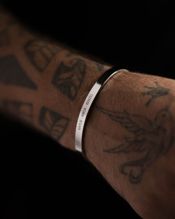 MARS Armband aus silberfarbenem Edelstahl mit der Gravur "Kaylie – Knox – Kenzo" am tätowierten Männerarm