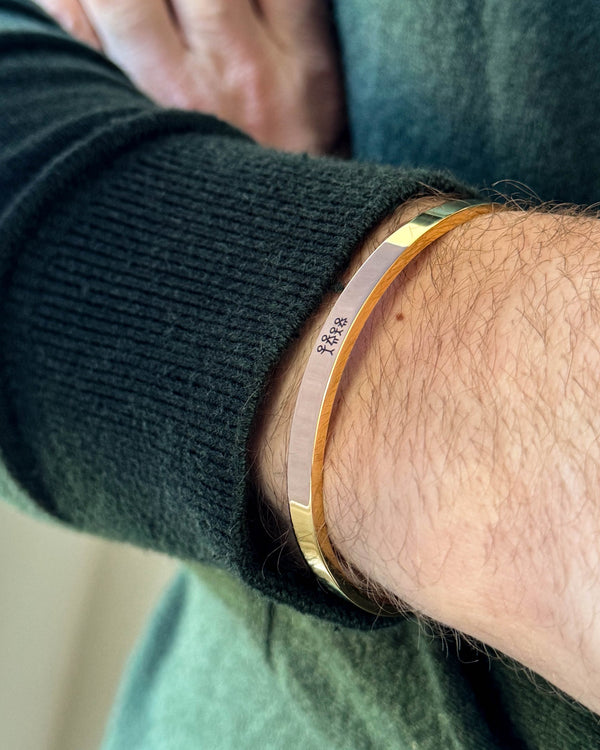 MARS STICK Armband aus vergoldetem Edelstahl mit gravierter Streichholz-Familie, am Handgelenk zu dunkelgrünem Strick getragen