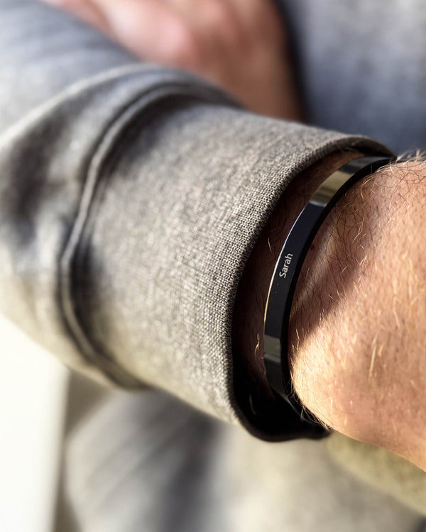 MARS Armband aus schwarzem Edelstahl mit graviertem Namen "Sarah" am Handgelenk eines Mannes, graues Sweatshirt