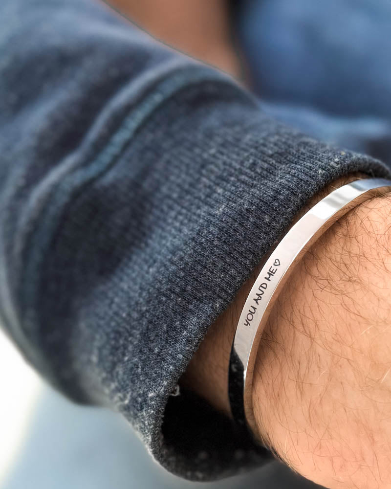 MARS SCRIPT Armband aus silberfarbenem Edelstahl mit "You and me" ♡ in Handschrift graviert, am Handgelenk, blaues Sweatshirt