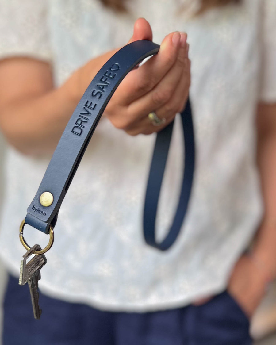 MAX Schlüsselanhänger aus dunkelblauem Leder als lange Schlaufe mit Messingniete und der Gravur "Drive safe" ♡, in der Hand gehalten mit Schlüssel