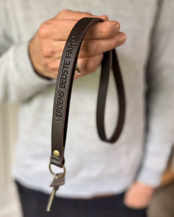 MAX Schlüsselanhänger aus dunkelbraunem Leder als lange Schlaufe mit der Gravur "Verdens bedste far" ♡, in der Hand gehalten mit Schlüssel