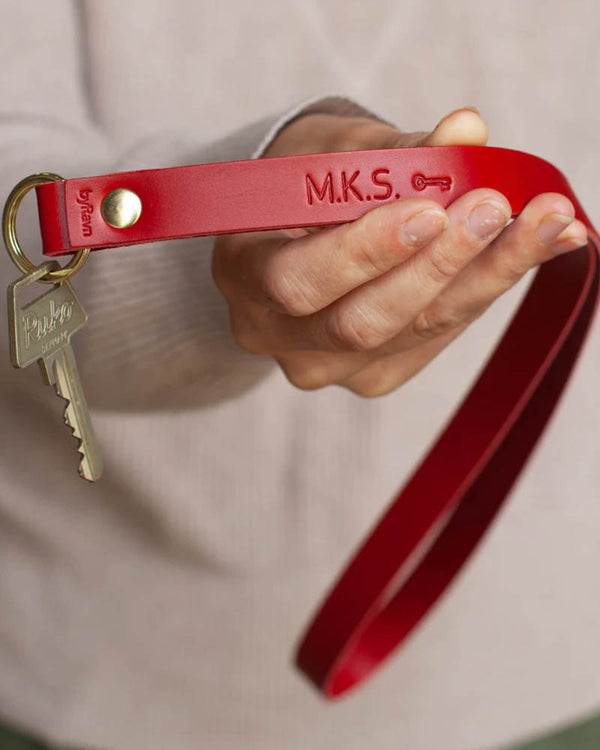 MAX Schlüsselanhänger aus rotem Leder als lange Schlaufe mit gravierten Initialen "M.K.S." und Schlüsselsymbol, in der Hand gehalten mit Schlüssel