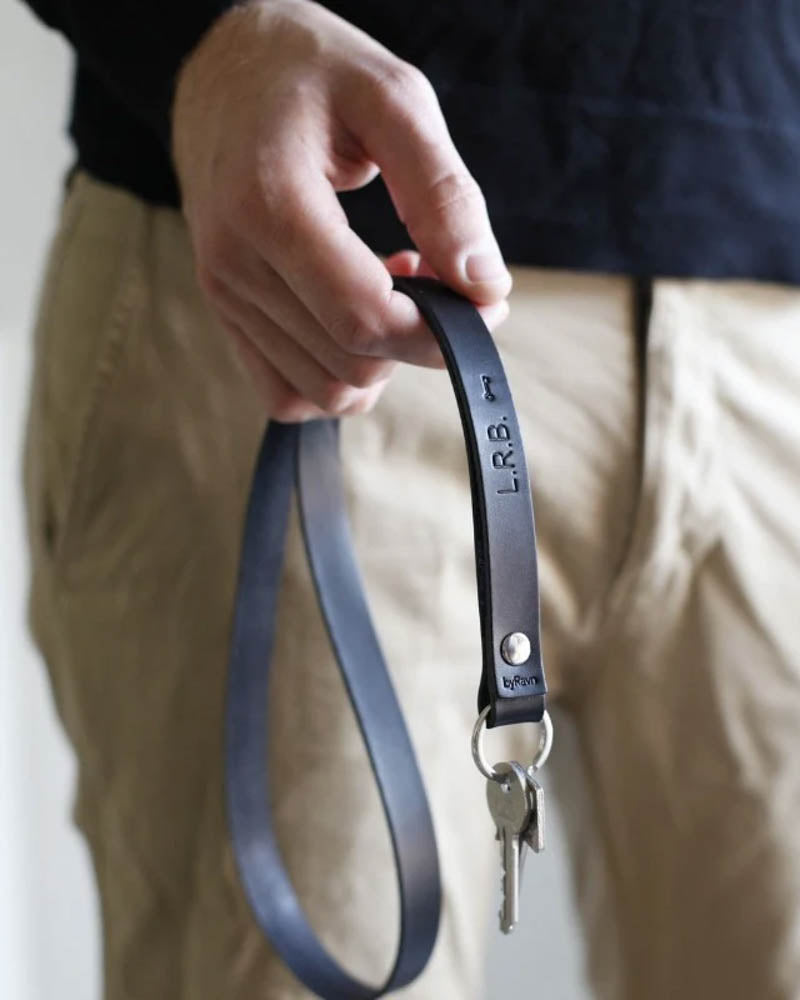 MAX Schlüsselanhänger aus schwarzem Leder mit gravierten Initialen "L.R.B." und kleinem Schlüsselsymbol, lange Schlaufe in der Hand mit Schlüsseln