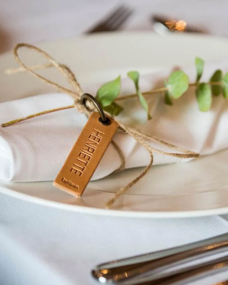 Muster der MERRY Tischkarte aus naturfarbenem Leder mit graviertem Namen "Henriette", um Serviette mit Eukalyptus gebunden