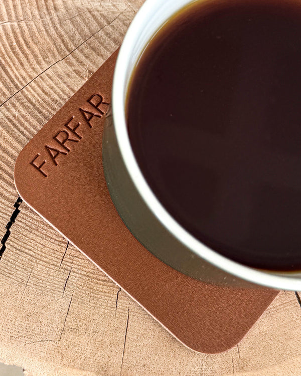 MOKKA quadratischer Untersetzer aus Leder in Cognac mit der Gravur "Farfar" unter Kaffeetasse auf Holzscheibe