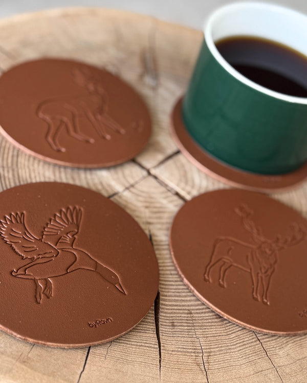 MOKKA Jagd-Untersetzer aus cognacfarbenem Leder mit geprägter fliegender Stockente, Rehbock und Rothirsch auf Holzscheibe mit grüner Kaffeetasse