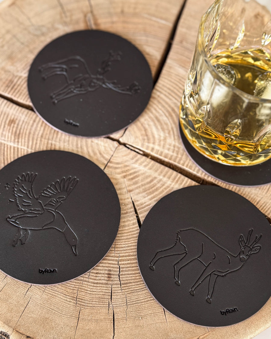 MOKKA Jagd-Untersetzer aus dunkelbraunem Leder mit geprägter Stockente, Rehbock und Rothirsch auf Holzscheibe neben Whiskyglas