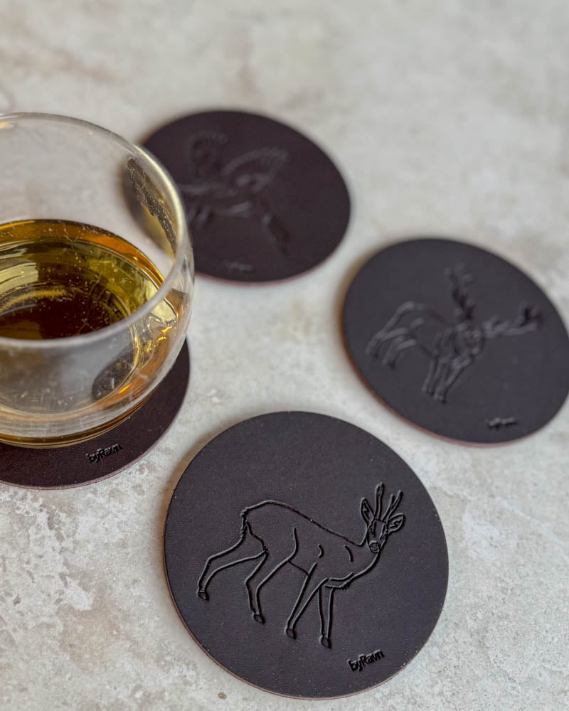 MOKKA Jagd-Untersetzer aus dunkelbraunem Leder mit geprägtem Rehbock, Stockente und Rothirsch auf hellem Tisch neben Glas Whisky