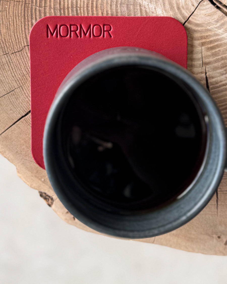 MOKKA quadratischer Untersetzer aus rotem Leder mit der Gravur "Mormor" unter schwarzer Kaffeetasse auf Holzscheibe, von oben