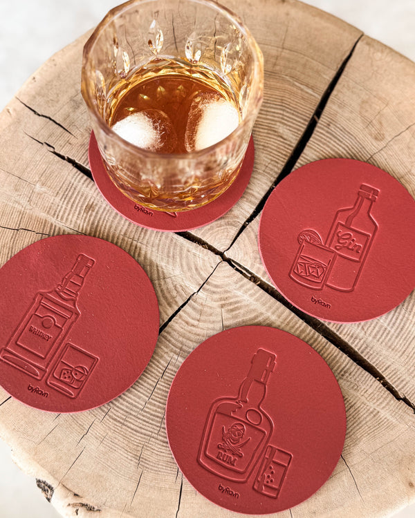 MOKKA Untersetzer aus rotem Leder, geprägt mit Whisky, Gin und Rum, auf Holzscheibe neben Kristallglas mit Whisky und Eis