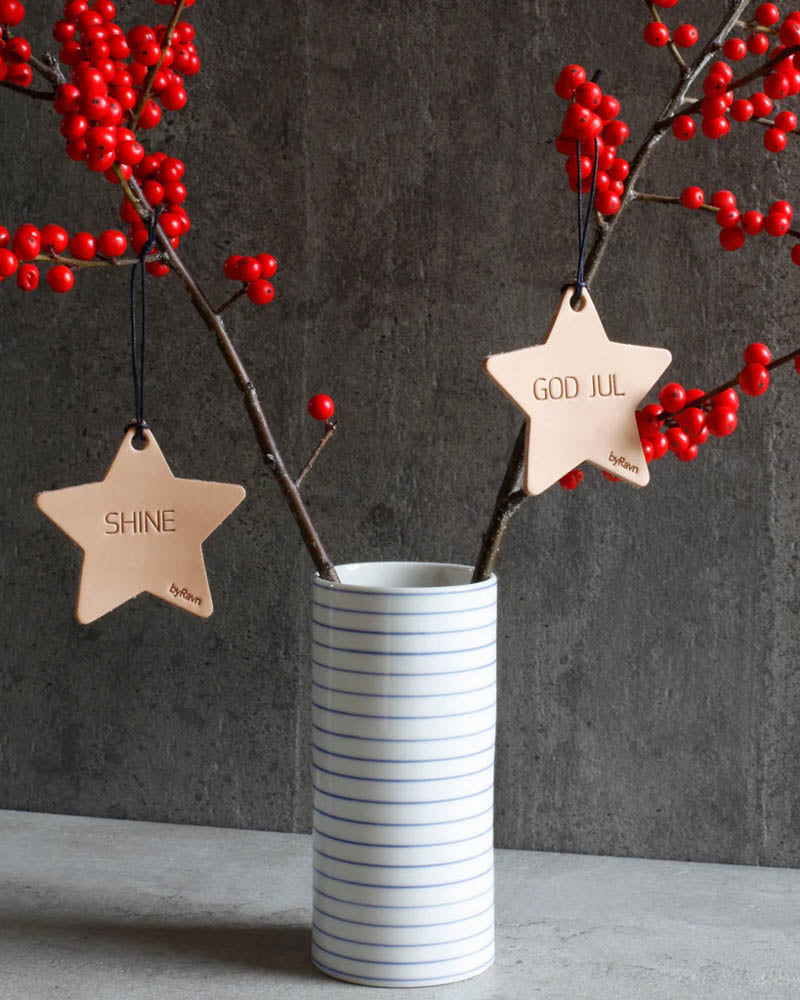 NORTH Weihnachtssterne aus naturfarbenem Leder mit den Gravuren "Shine" und "God jul" an Zweigen mit roten Beeren in gestreifter Vase