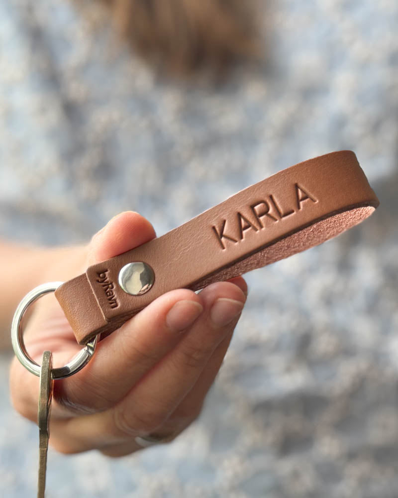 RAVN Schlüsselanhänger aus Cognac-Leder mit dem gravierten Namen "Karla", in der Hand gehalten