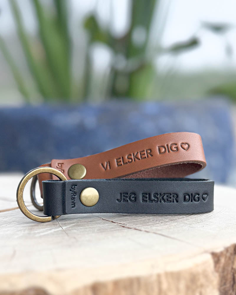 RAVN Schlüsselanhänger aus Cognac- und schwarzem Leder auf Holzscheibe mit den Gravuren "Vi elsker dig" ♡ und "Jeg elsker dig" ♡
