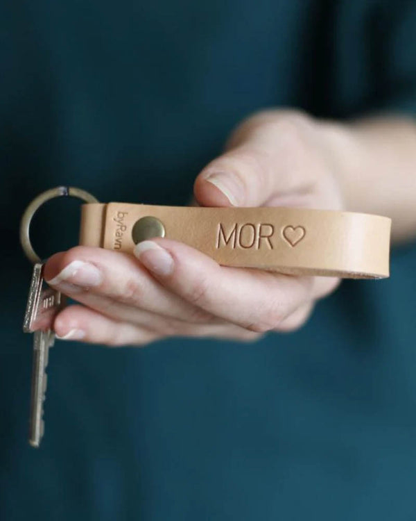 RAVN Schlüsselanhänger aus naturfarbenem Leder mit der Gravur "Mor" ♡, in der Hand gehalten mit Schlüsseln