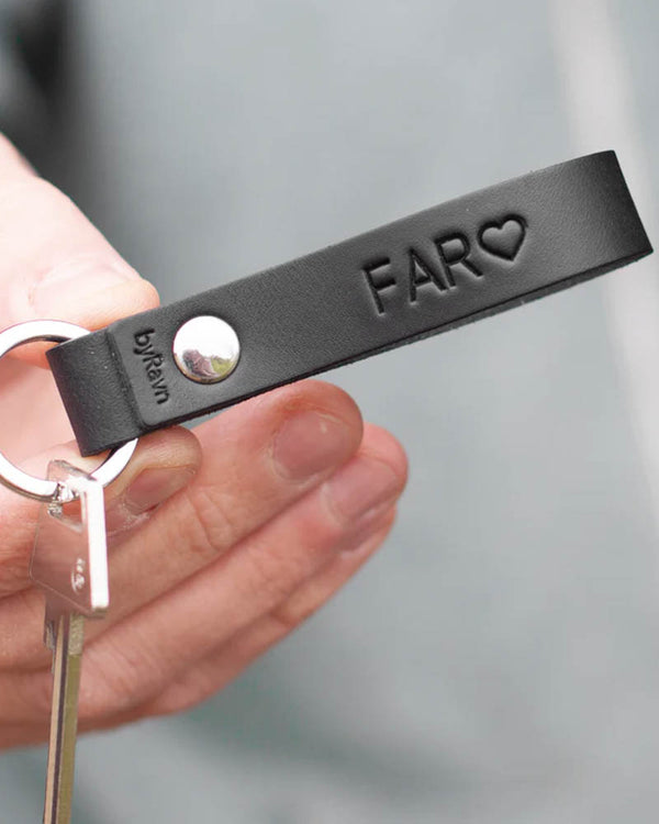 RAVN Schlüsselanhänger aus schwarzem Leder mit der Gravur "Far" ♡ und Niete aus Stahl, in der Hand gehalten mit Schlüssel