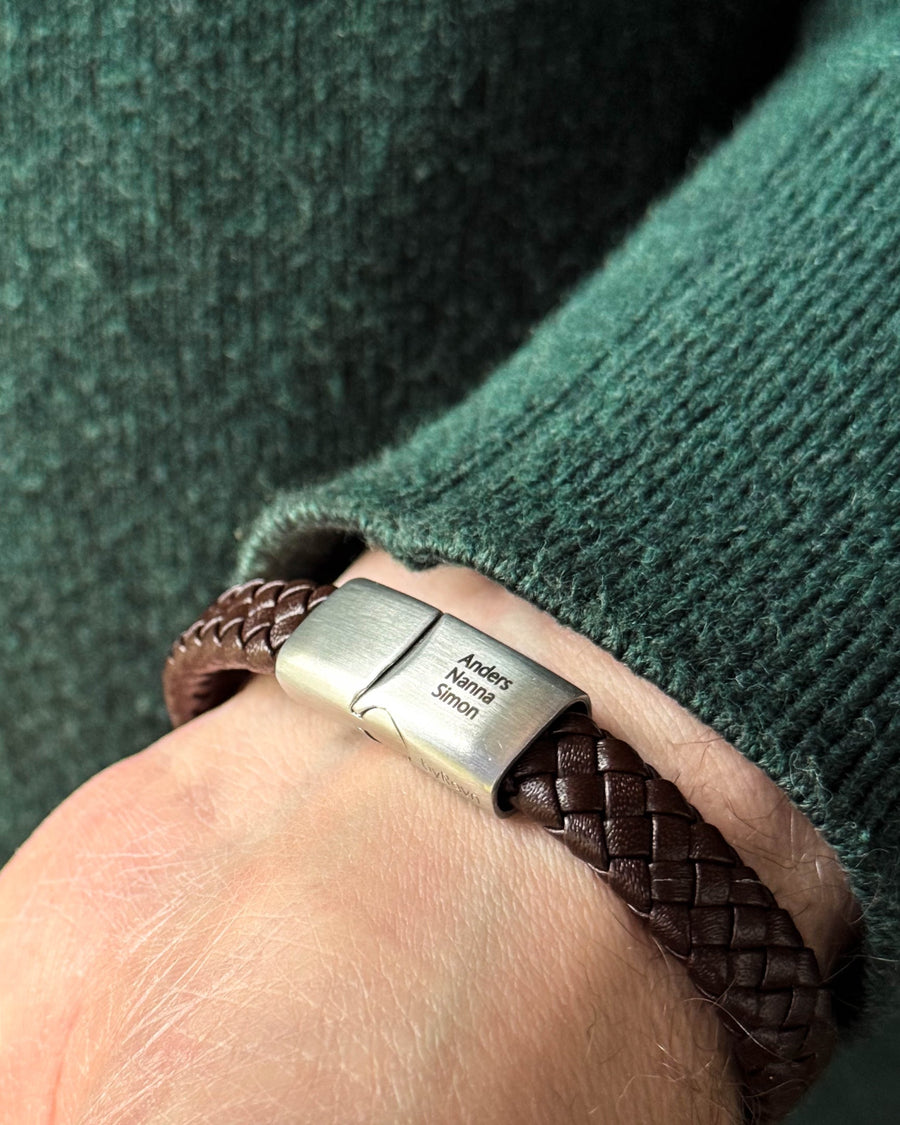 RAY Lederarmband aus dunkelbraunem geflochtenem Leder mit den Namen "Anders, Nanna, Simon" auf dem Edelstahlverschluss graviert, zu grünem Strick