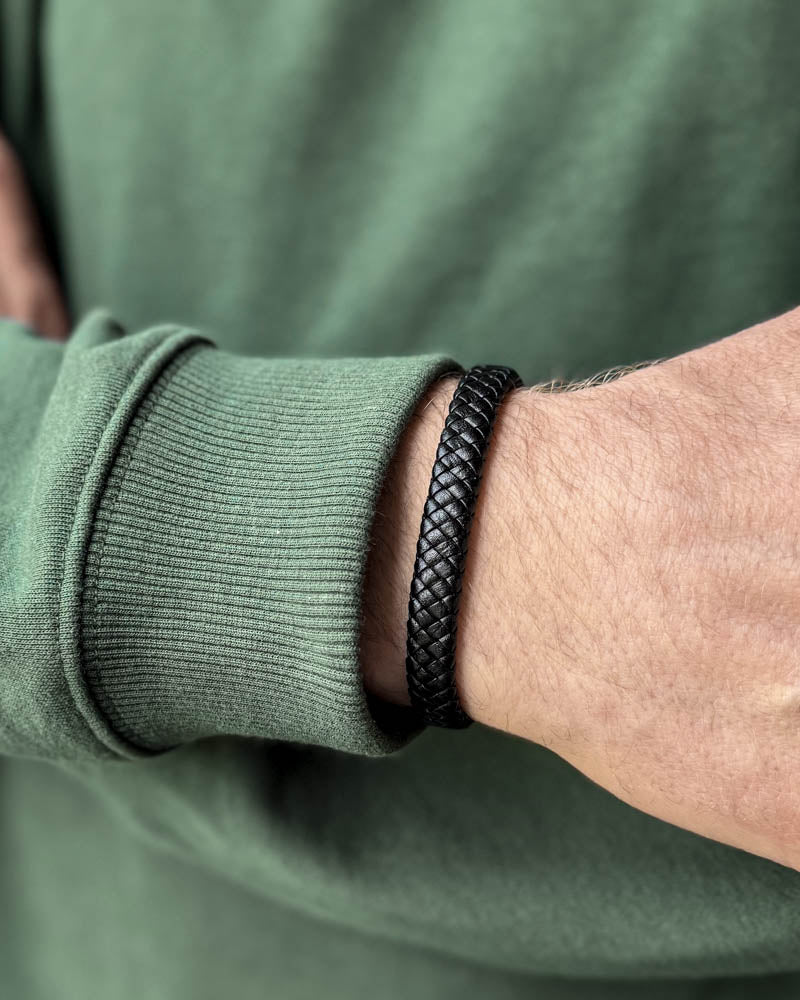 RAY Lederarmband aus schwarzem geflochtenem Leder am Handgelenk eines Mannes, grünes Sweatshirt