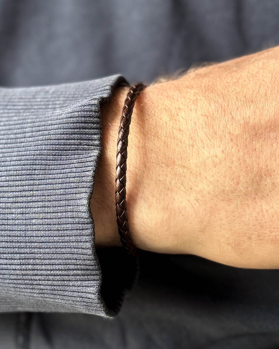 RIO Lederarmband aus dunkelbraunem geflochtenem Leder am Handgelenk eines Mannes, blaugraues Sweatshirt