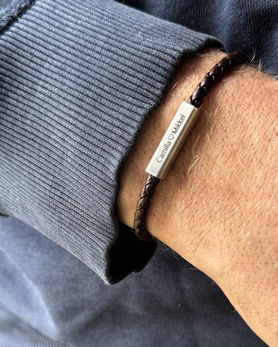 RIO Lederarmband aus dunkelbraunem geflochtenem Leder mit "Camilla ♡ Mikkel" auf dem Edelstahlverschluss graviert, am Handgelenk getragen