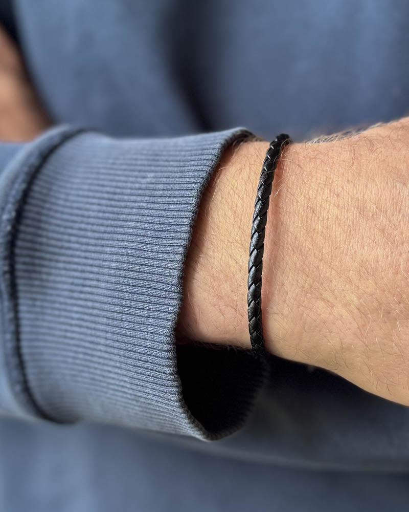 RIO Lederarmband aus schwarzem geflochtenem Leder am Handgelenk eines Mannes, blaugraues Sweatshirt
