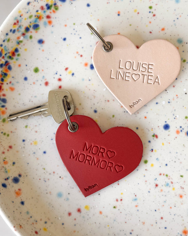 ROSE Herz-Schlüsselanhänger aus naturfarbenem und rotem Leder mit den Gravuren "Louise Line ♡ Tea" und "Mor ♡ Mormor ♡" auf gepunktetem Teller