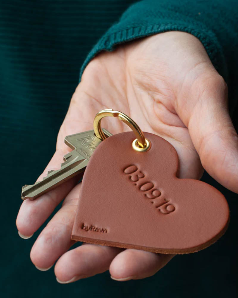ROSE Herz-Schlüsselanhänger aus Leder in Cognac, in der Hand gehalten, mit Schlüssel und dem gravierten Datum "03.09.19"
