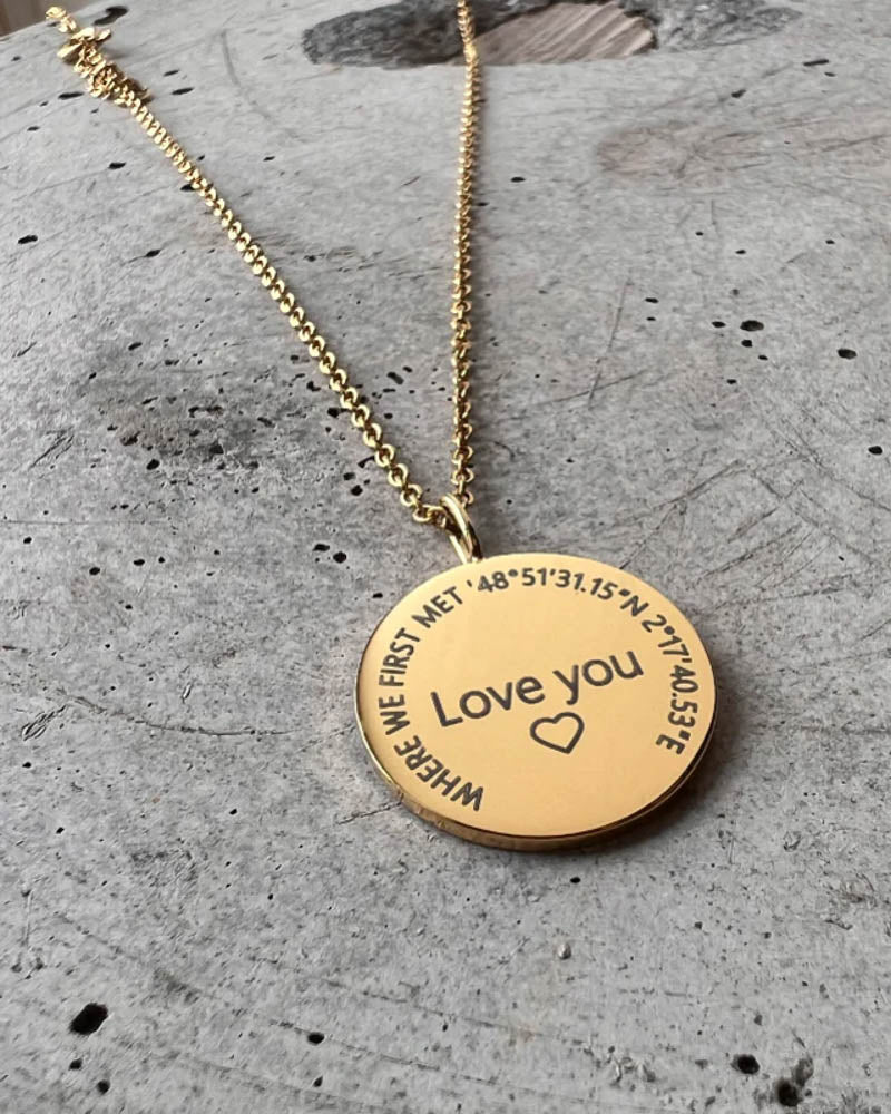 SIA CIRCLE Halskette aus vergoldetem Edelstahl mit "Love you" ♡ und "Where we first met" mit Koordinaten im Kreis graviert, auf Beton