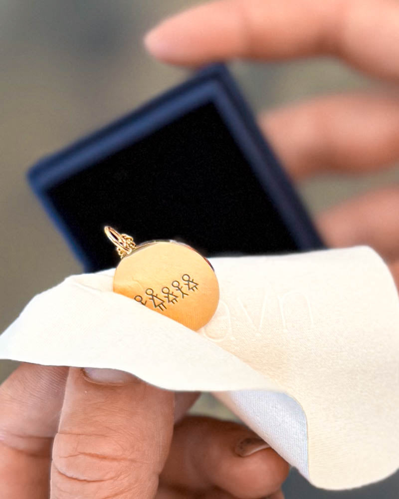 SIA STICK Halskette aus vergoldetem Edelstahl mit gravierter Streichholz-Familie, in der Hand gehalten auf Putztuch neben der Geschenkbox