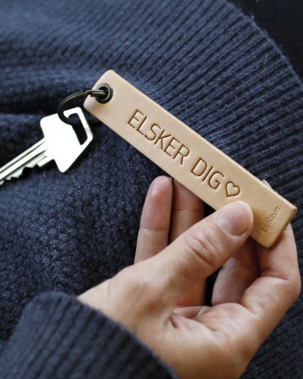 SOLO Medium Schlüsselanhänger aus naturfarbenem Leder, in der Hand gehalten, mit Schlüssel und der Gravur "Elsker dig" ♡